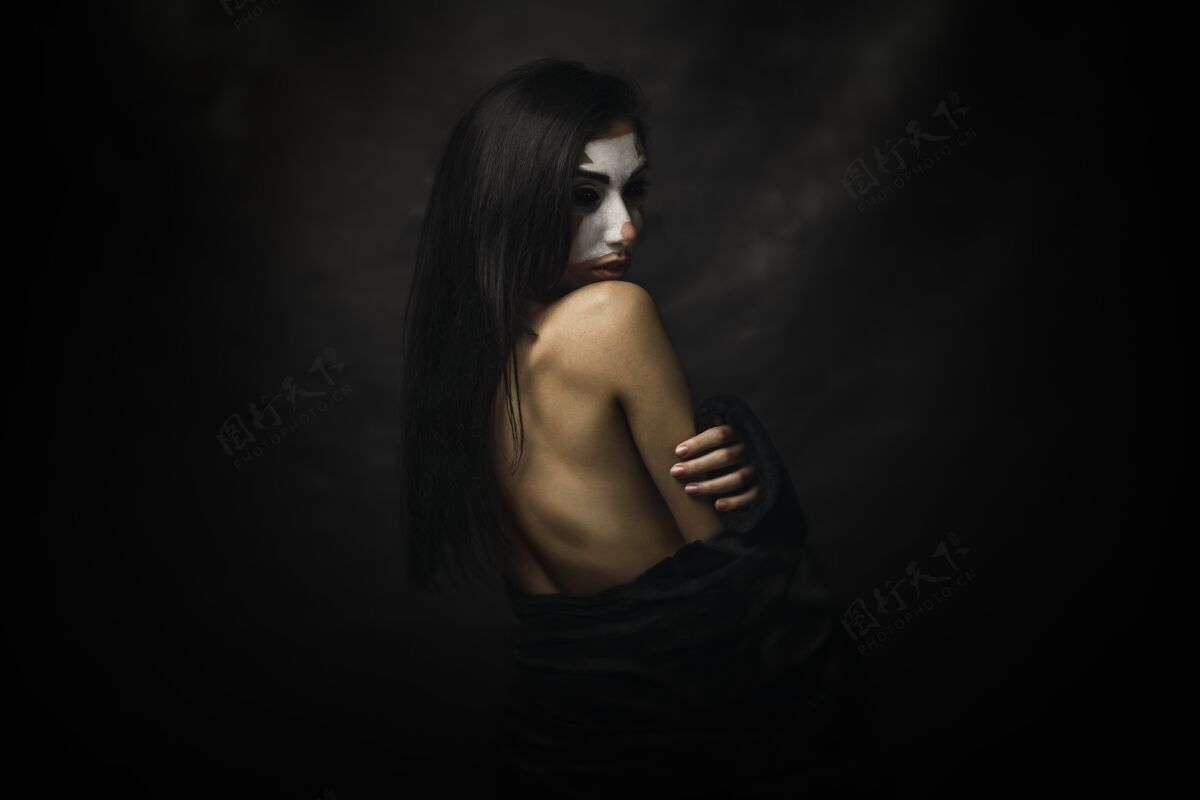 脸半裸的女人脸上涂着小丑妆站在黑色背景前美女幽默服装