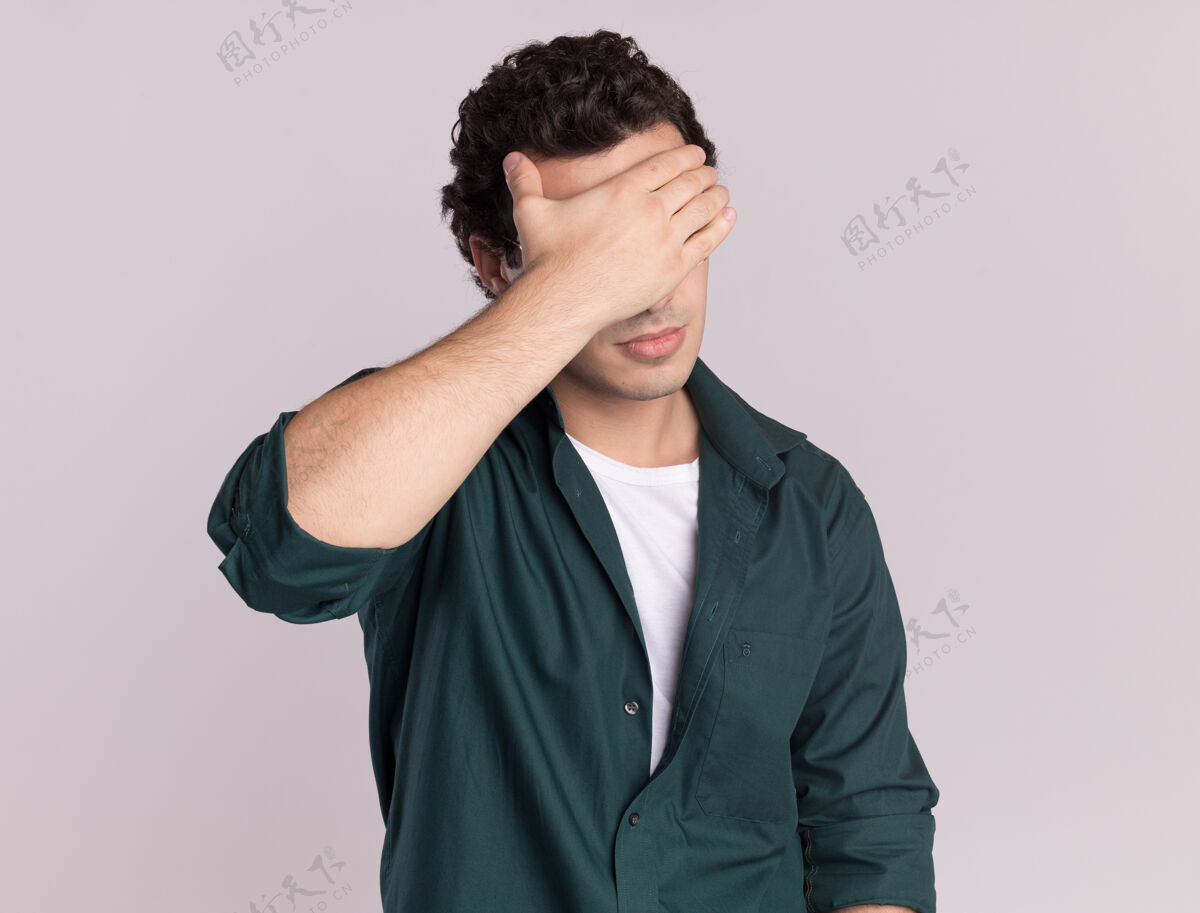 站着穿绿衬衫的年轻人累了 无聊地闭上眼睛 手站在白墙上眼睛封闭年轻