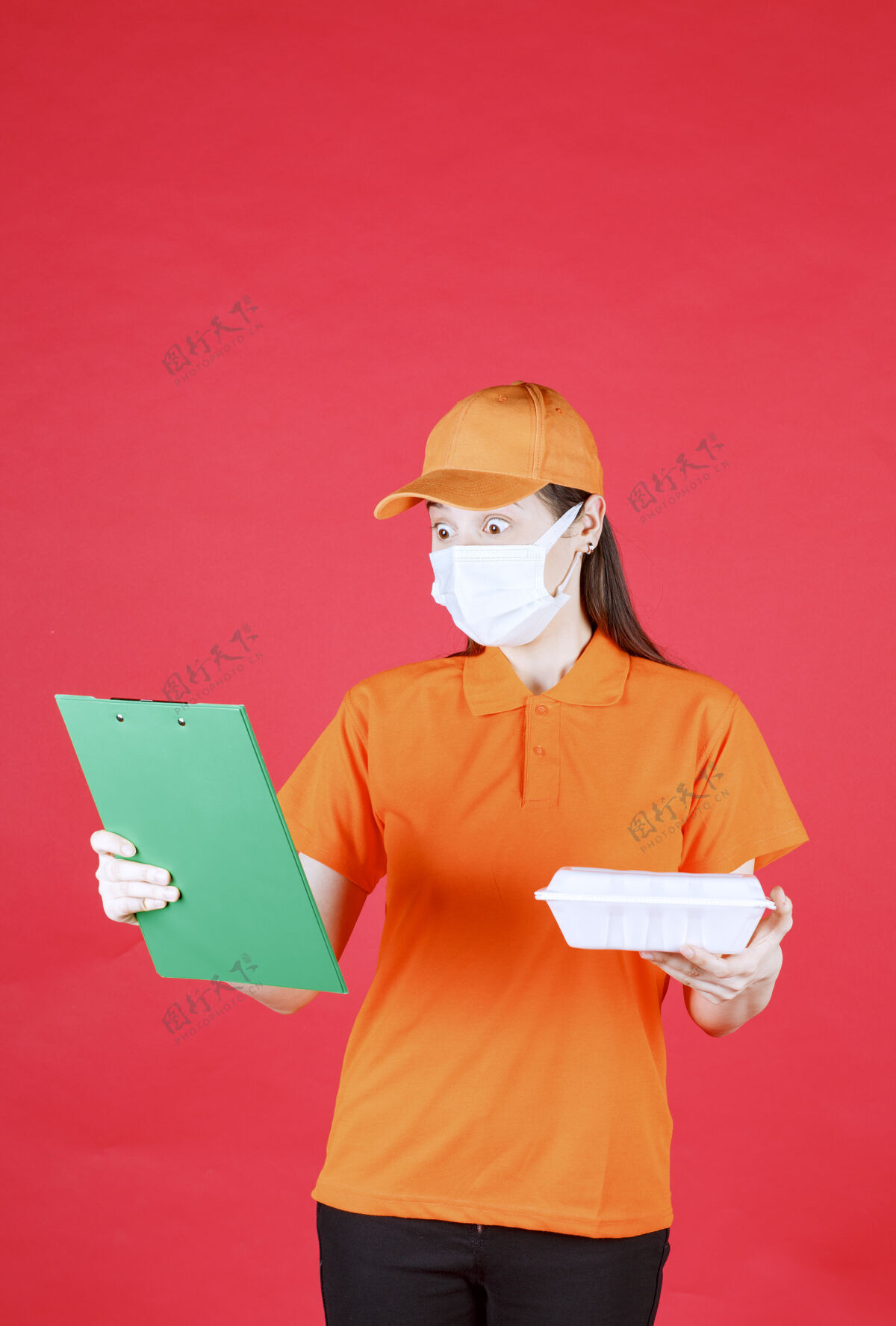 阅读身着橙色制服和口罩的女服务人员手持外卖食品包 检查绿色文件夹年轻人制服送货员
