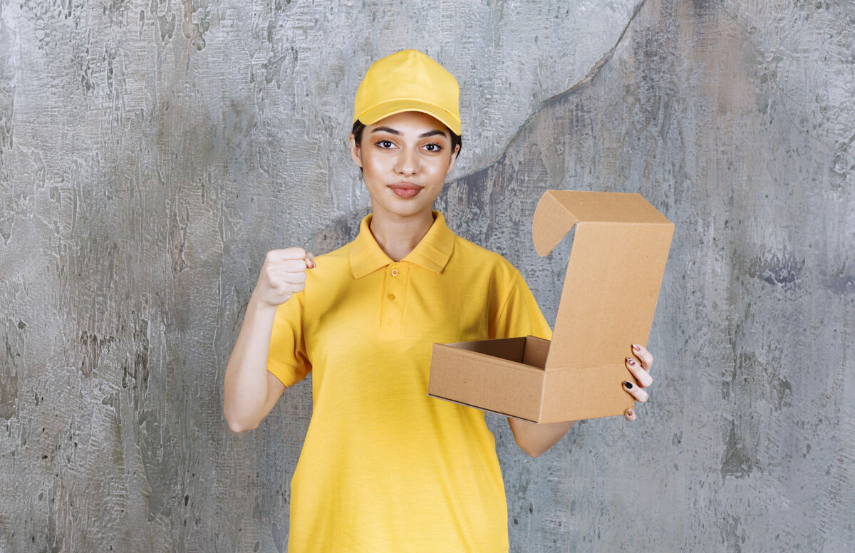成人穿着黄色制服的女服务人员手持一个打开的纸板箱 并显示积极的手势外卖工人快递