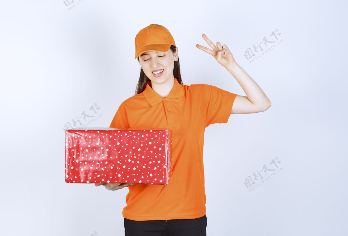 年轻人身着橙色制服的女服务人员手持红色礼盒 手持和平标志女士朋友礼品盒