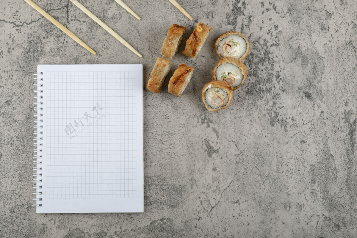 顶视图用筷子和笔记本在石头背景上炸寿司面包光卷