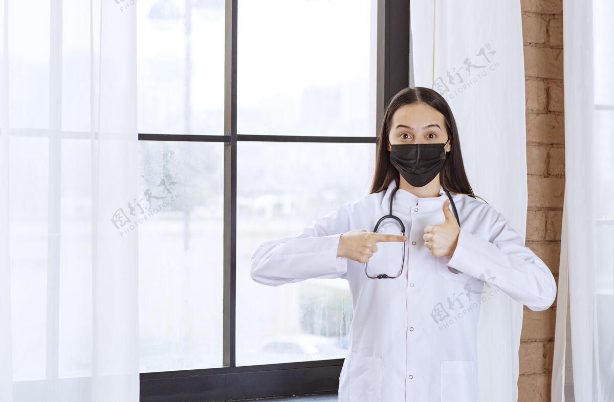 诊所戴着黑色口罩的医生站在窗边 带着听诊器 并显示出满意的迹象细菌病毒医学