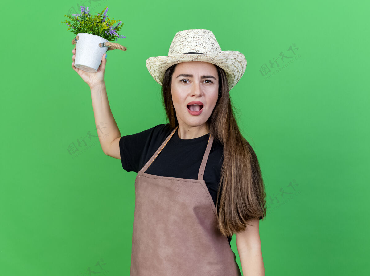 花盆一个穿着制服的漂亮园丁女孩戴着园艺帽 在绿色的背景下孤立地在花盆里养花帽子女孩惊喜