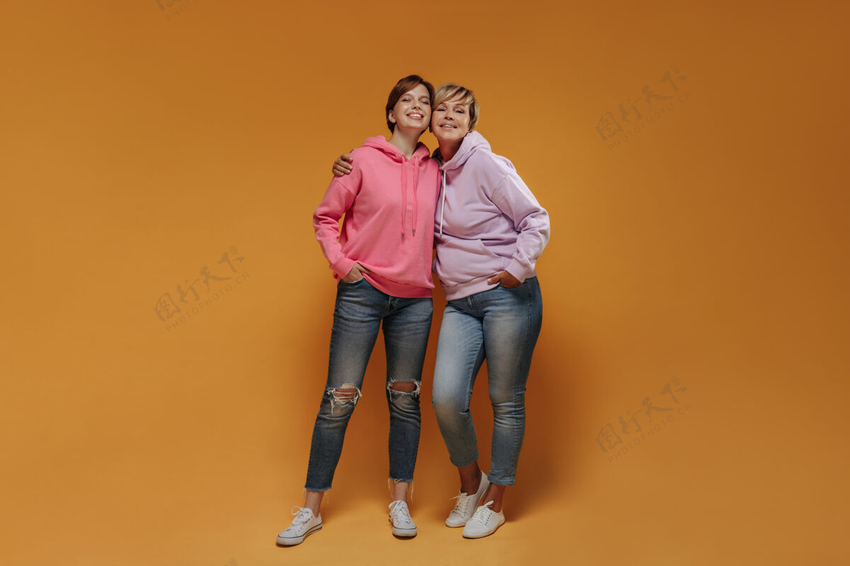 女儿现代的两个女人 一头酷酷的短发 穿着粉色宽边连帽衫 紧身牛仔裤和白色运动鞋 面带微笑地看着镜头牛仔裤衬衫成人
