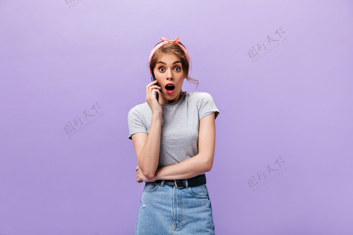 衬衫穿着灰色衬衫的惊艳女士在电话里交谈穿着黑色腰带牛仔裙的惊艳年轻女士在紫色背景上摆姿势紫色肖像时尚