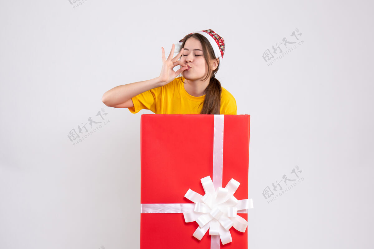 购物者前视图可爱的女孩与圣诞老人帽子站在大礼物后面微笑站购物
