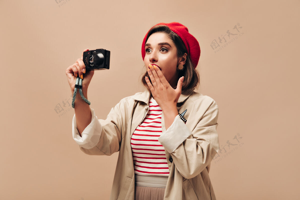 红唇穿着红色贝雷帽和时髦外套的女士拿着相机穿着条纹毛衣和轻便外套的可爱女士在孤立的背景下摆姿势贝雷帽姿势肖像