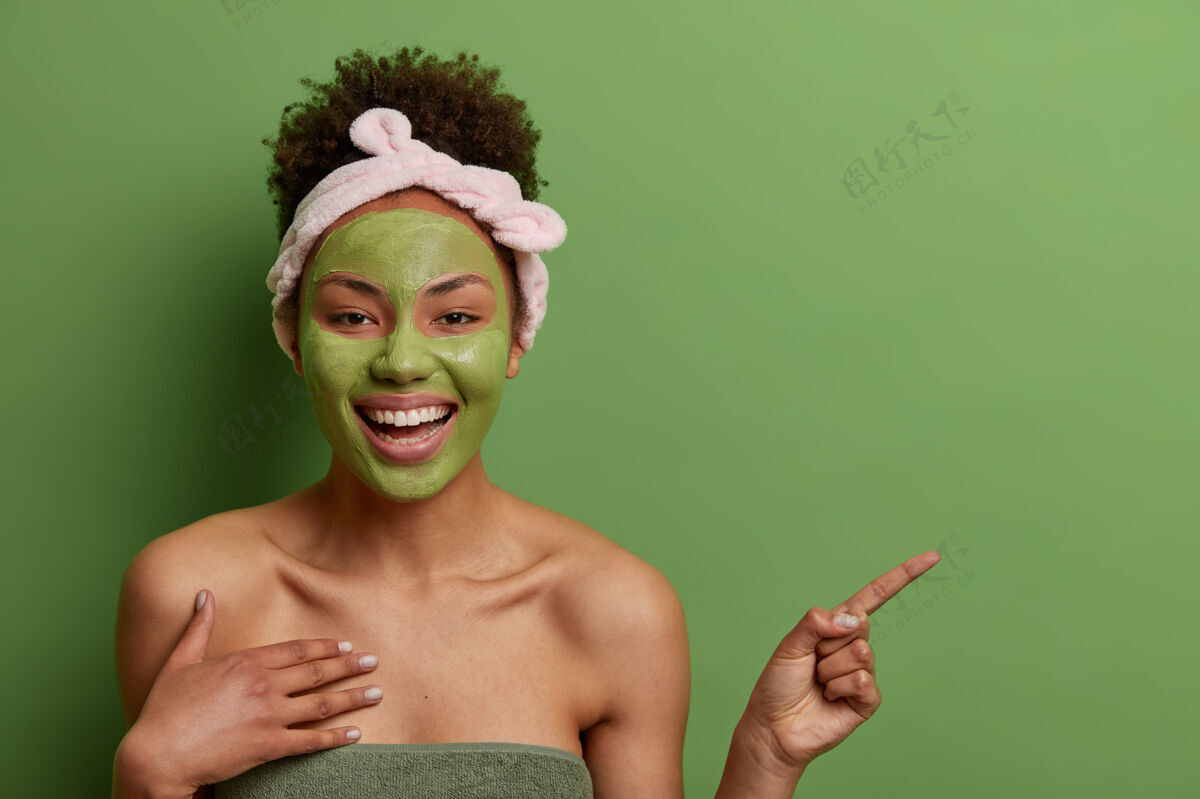 肖像帅气开朗的美国黑人女性镜头在脸上敷美容面膜 推荐美容产品 在复制空间上标明 隔离在绿色墙壁上护肤理念民族美容卷发