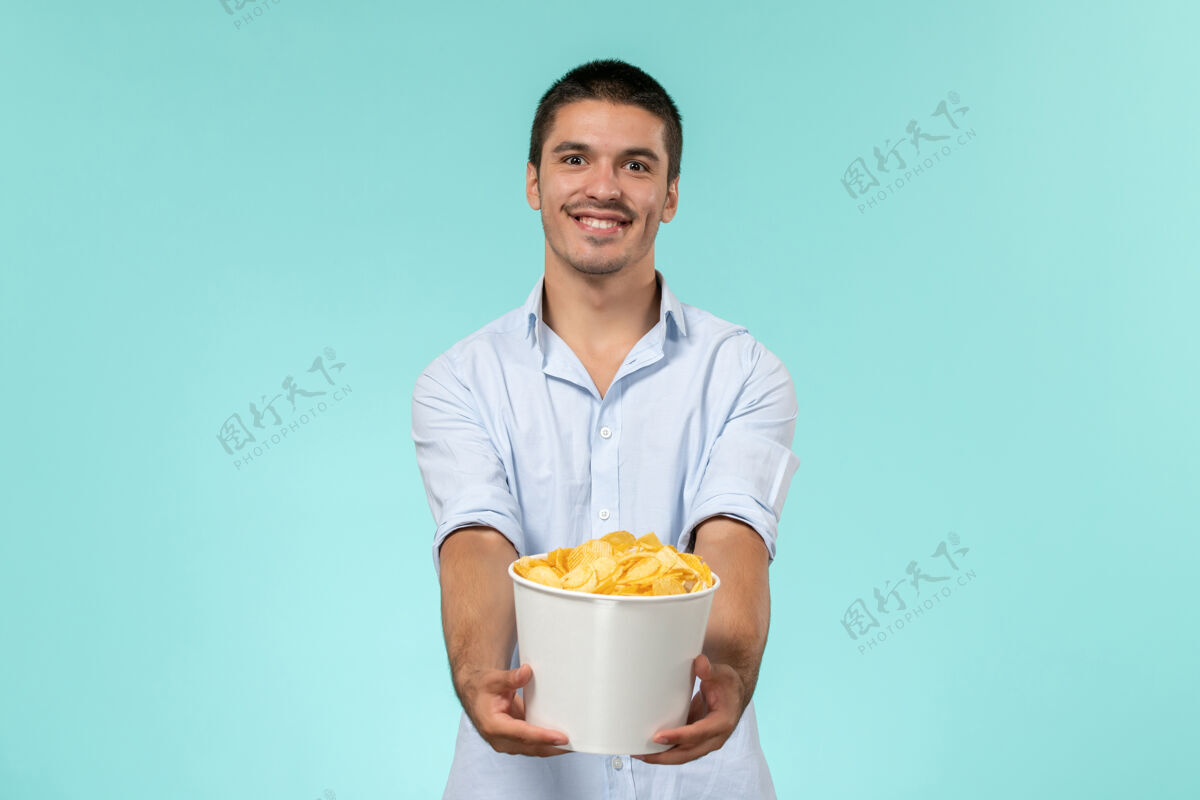 大人正面图：年轻人拿着篮子 手里拿着土豆 微笑着站在蓝色的墙上 孤独而遥远的男性电影院风景男人服务员