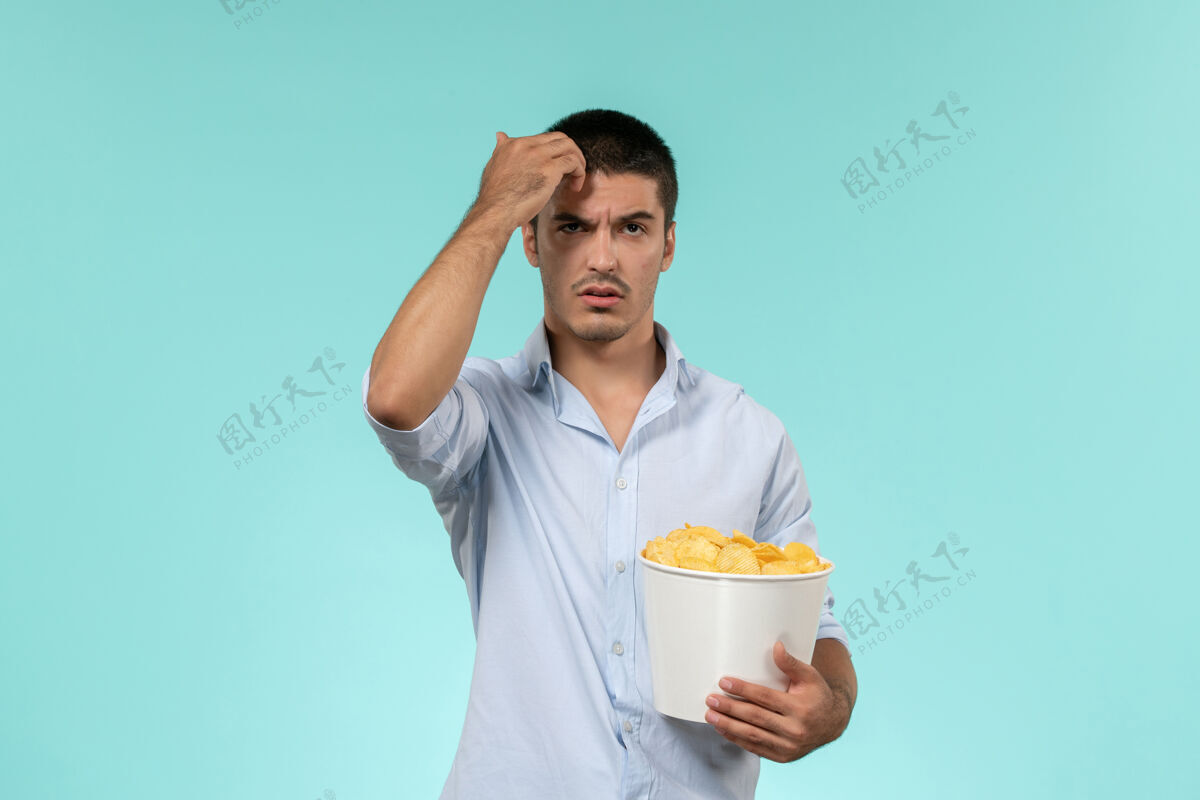 年轻人正面图：一个年轻人拿着土豆cips在一张蓝色的办公桌上孤独的遥远的男性电影院电影土豆电影院