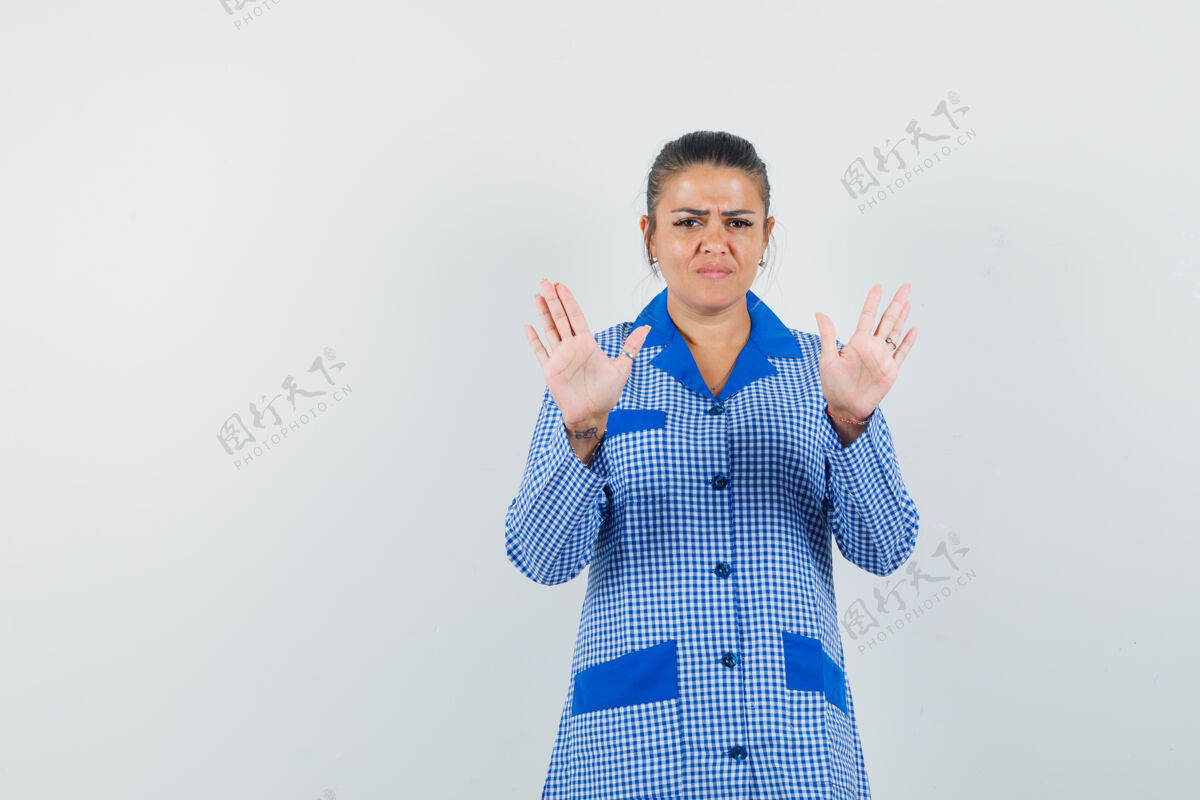 漂亮年轻女子显示停止标志 双手穿着蓝色方格布睡衣衬衫 表情严肃 正面视图睡衣前面干净