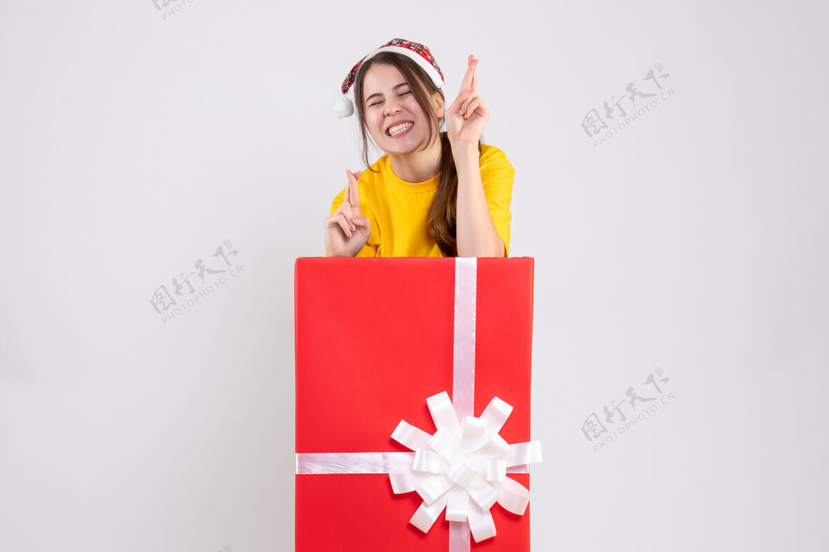 漂亮前视图兴高采烈的女孩戴着圣诞帽 站在大圣诞礼物后面祝你好运节日举行大