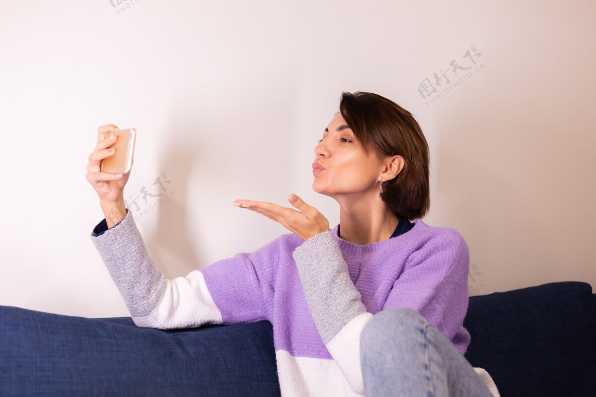 公寓年轻的白人女孩在卧室的沙发上看手机相机社交通话设备