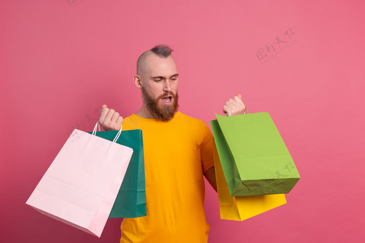 兴奋快乐的胡须积极的男人休闲装扮与五颜六色的购物袋工作室粉红色的背景购买男人成人