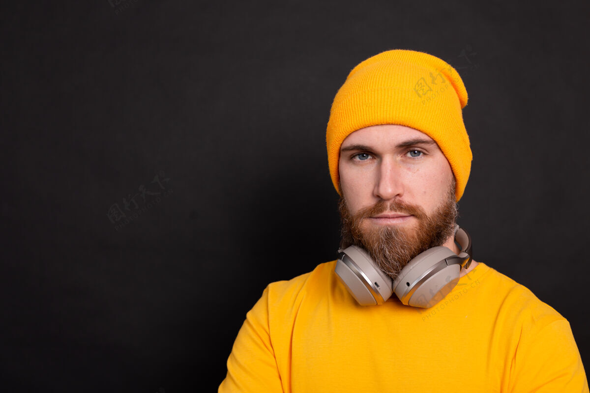 耳机帅气的大胡子时髦男人黄色帽子t恤 黑色背景上有独立的耳机男性黄色酷