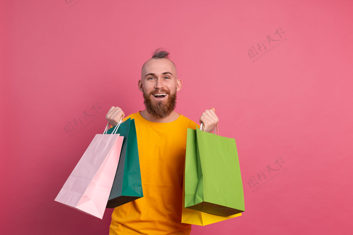 购买快乐的胡须积极的男人休闲装扮与五颜六色的购物袋工作室粉红色的背景好心情消费昂贵
