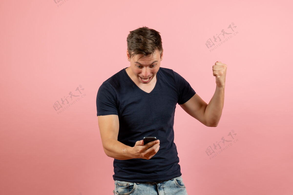 情感前视图身着蓝色t恤的年轻男性用手机在粉色背景上演绎男模情感色彩男成人人物男性