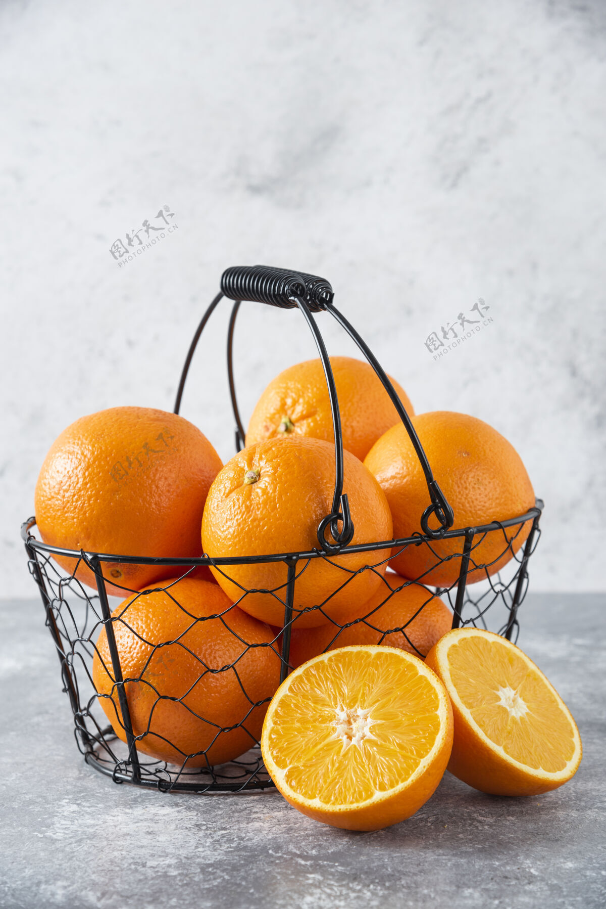 成熟石桌上放着一个装满多汁橙子的金属黑色篮子味道圆形多汁