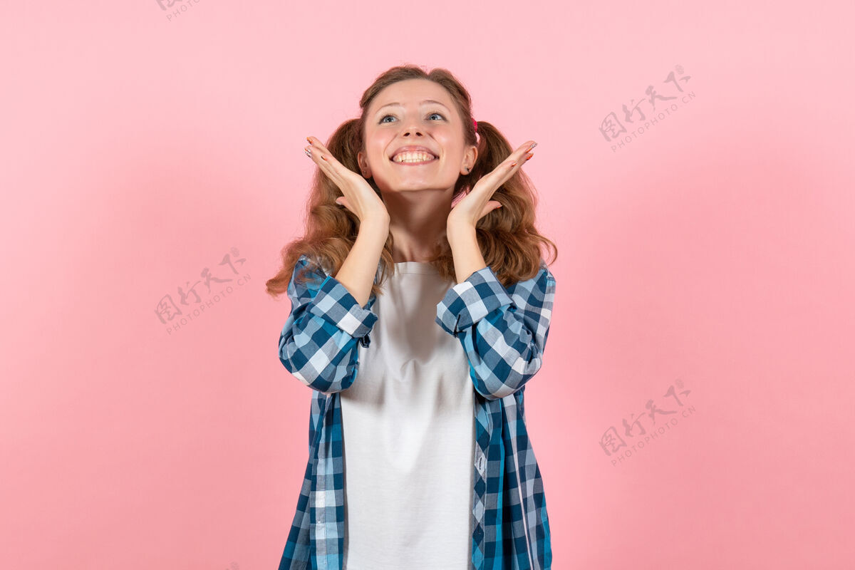 头发正面图身着蓝色格子衬衫的年轻女性在粉色背景上微微微笑摆姿势女性情感模特时尚女孩颜色人轻微年轻女性