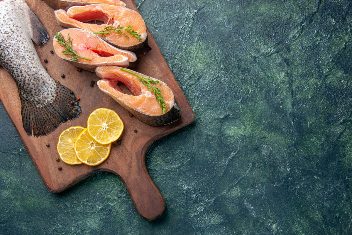 板新鲜生鱼片柠檬片绿色胡椒在深色桌子上的木质砧板上的水平视图切片混合烹饪