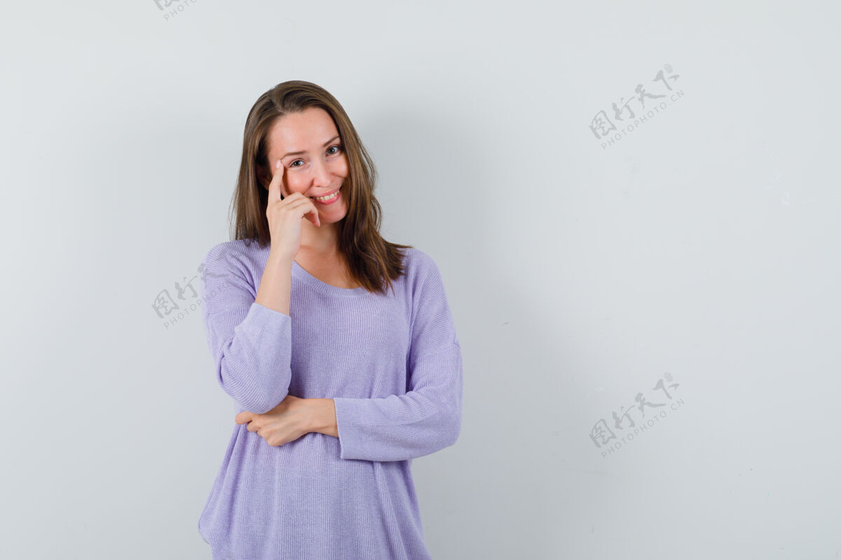 头发一个穿着淡紫色上衣的年轻女人 一边用手指按住太阳穴一边摆姿势 看上去很积极积极漂亮奢华