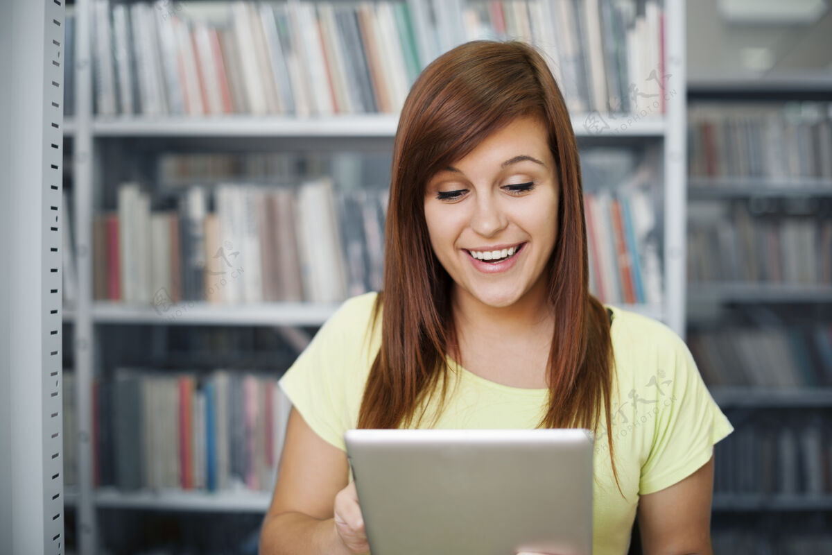 女性快乐的学生在图书馆使用数字平板电脑学生欢呼妇女