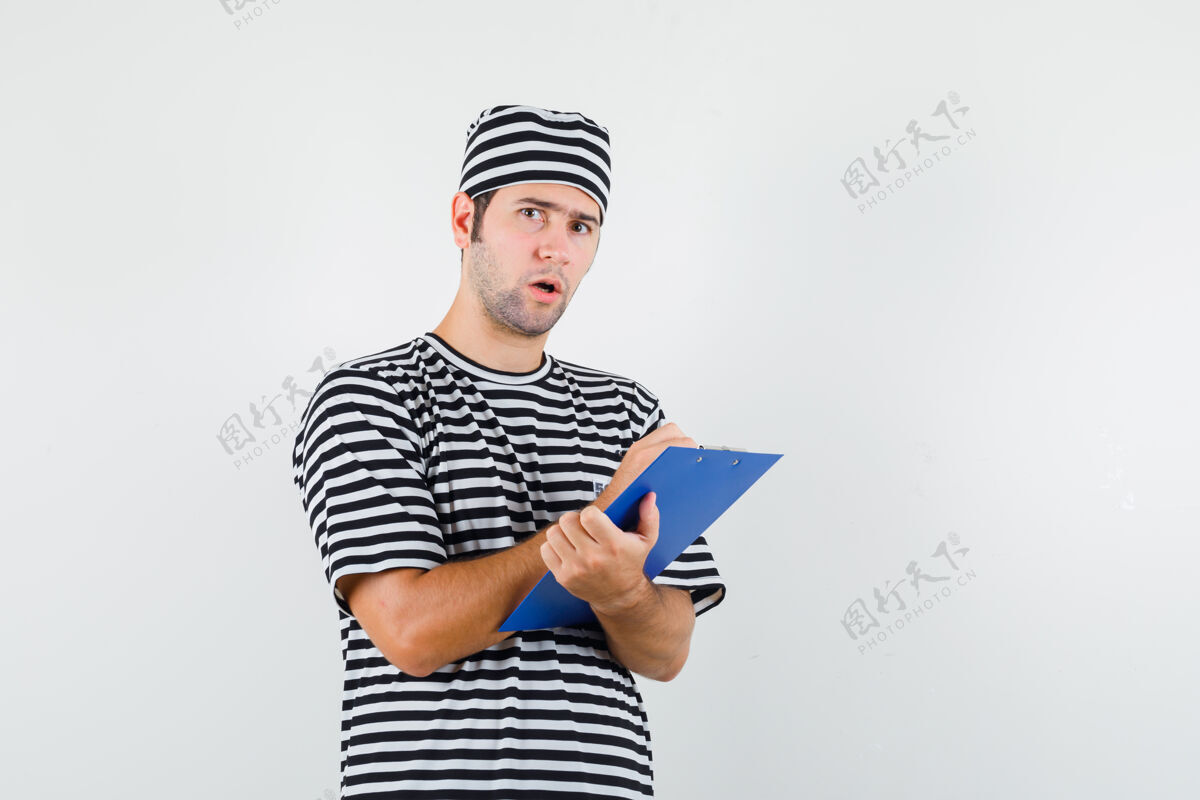 模特年轻男子穿着t恤 戴着帽子在剪贴板上记笔记 神情犹豫不决 俯视前方男性笔记胡子
