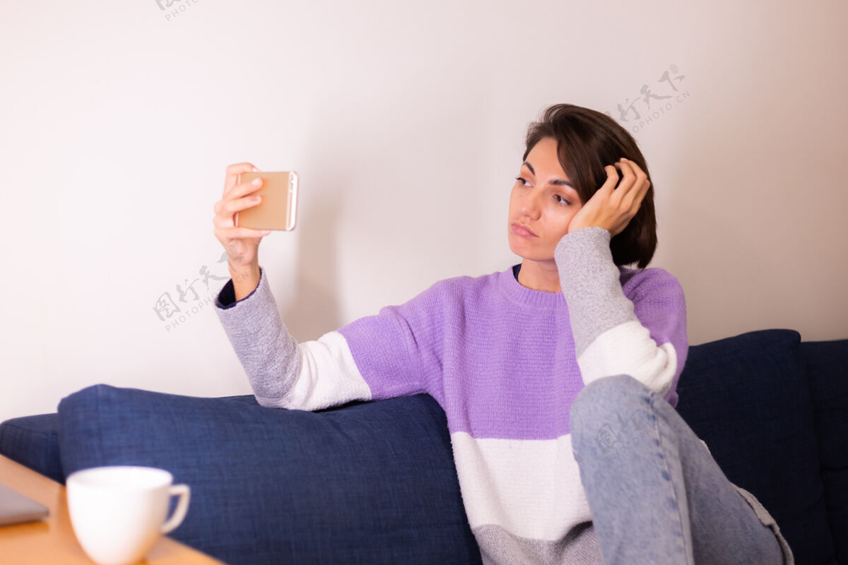 时间年轻的白人女孩在卧室的沙发上看手机相机无线人脸房子