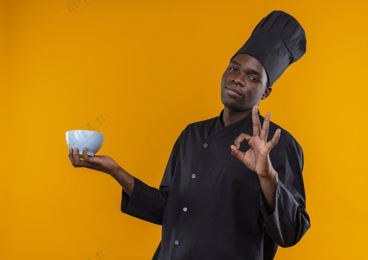 非裔美国人年轻自信的非洲裔美国厨师 身着厨师制服 手持碗 在橙色上做手势 并留有空白碗信心制服