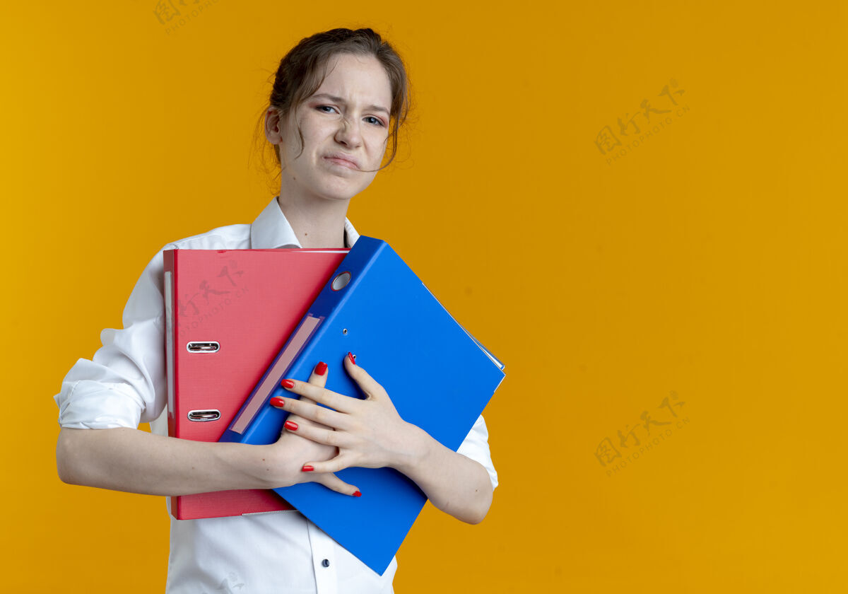 女孩年轻恼怒的金发俄罗斯女孩拿着文件夹在橙色的复制空间副本持有恼怒