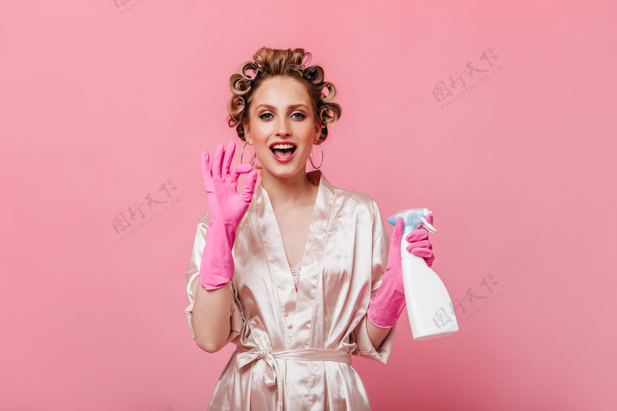 金发戴着粉色手套的家庭主妇拿着窗户清洁器 并显示ok标志人长袍肖像