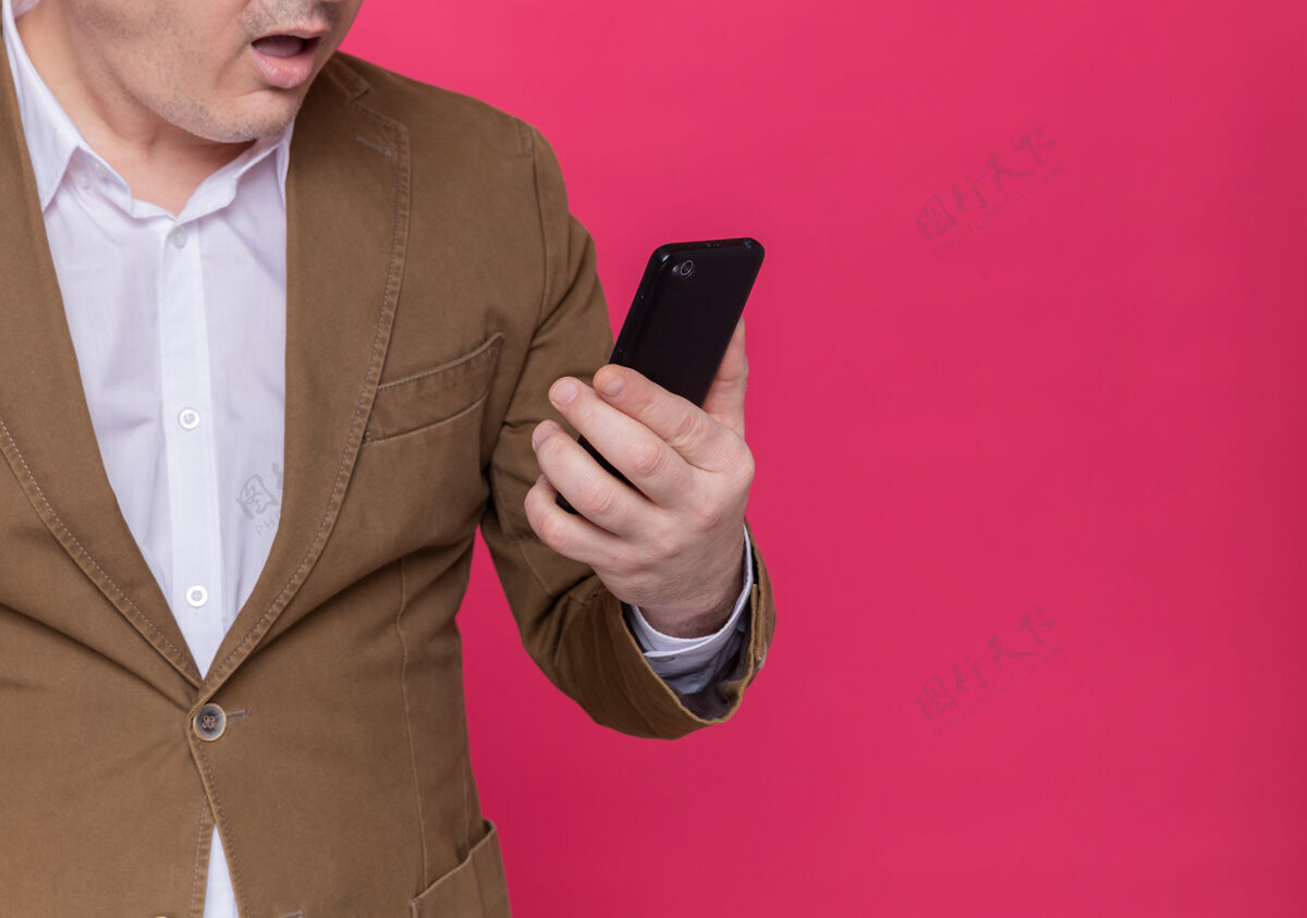 站着一张剪下来的照片 穿着西装的中年男子拿着手机看着它惊讶不已手机惊喜男人