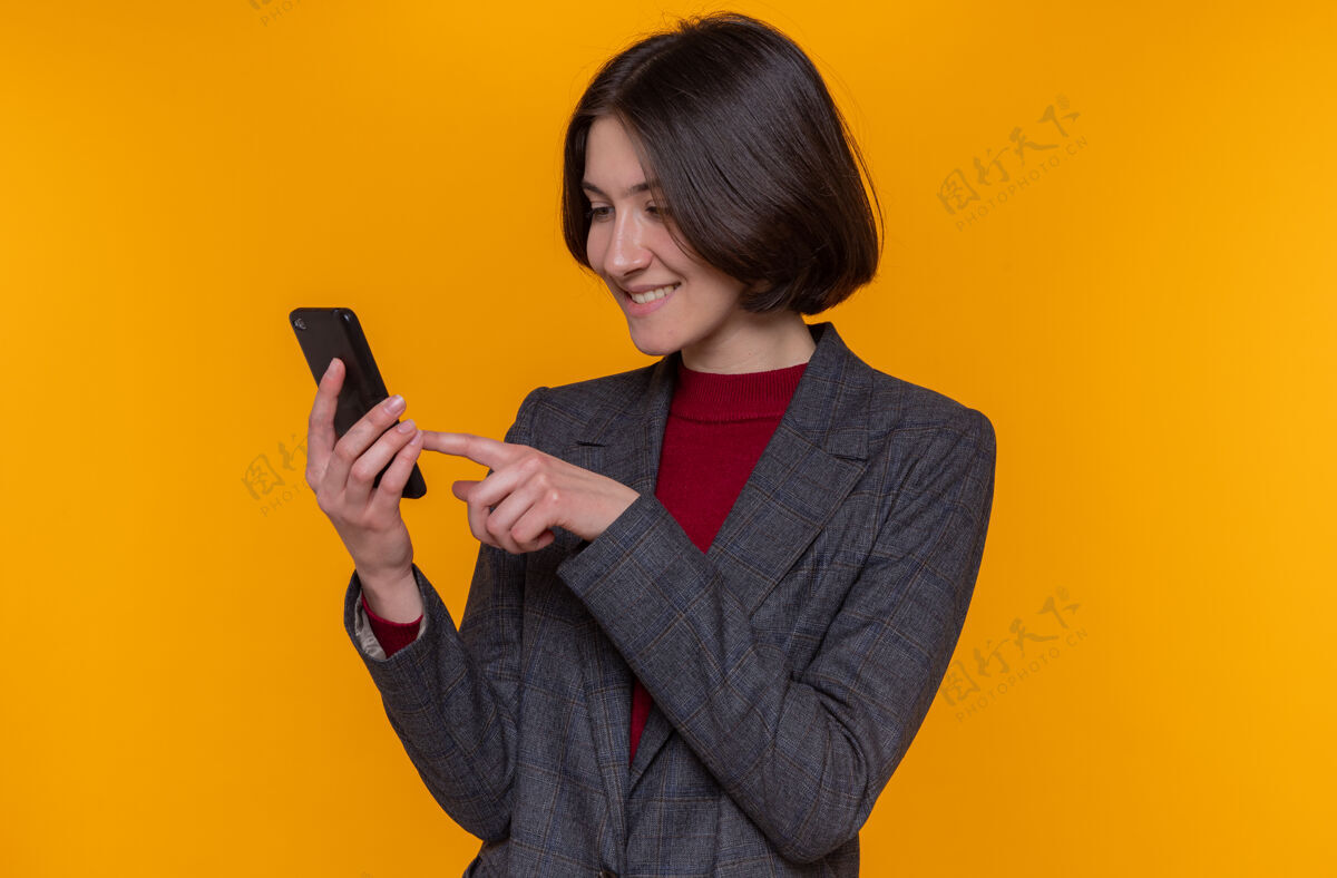 女士快乐的年轻女子 短发 身穿灰色夹克 手持智能手机 输入各种信息夹克支架短裤