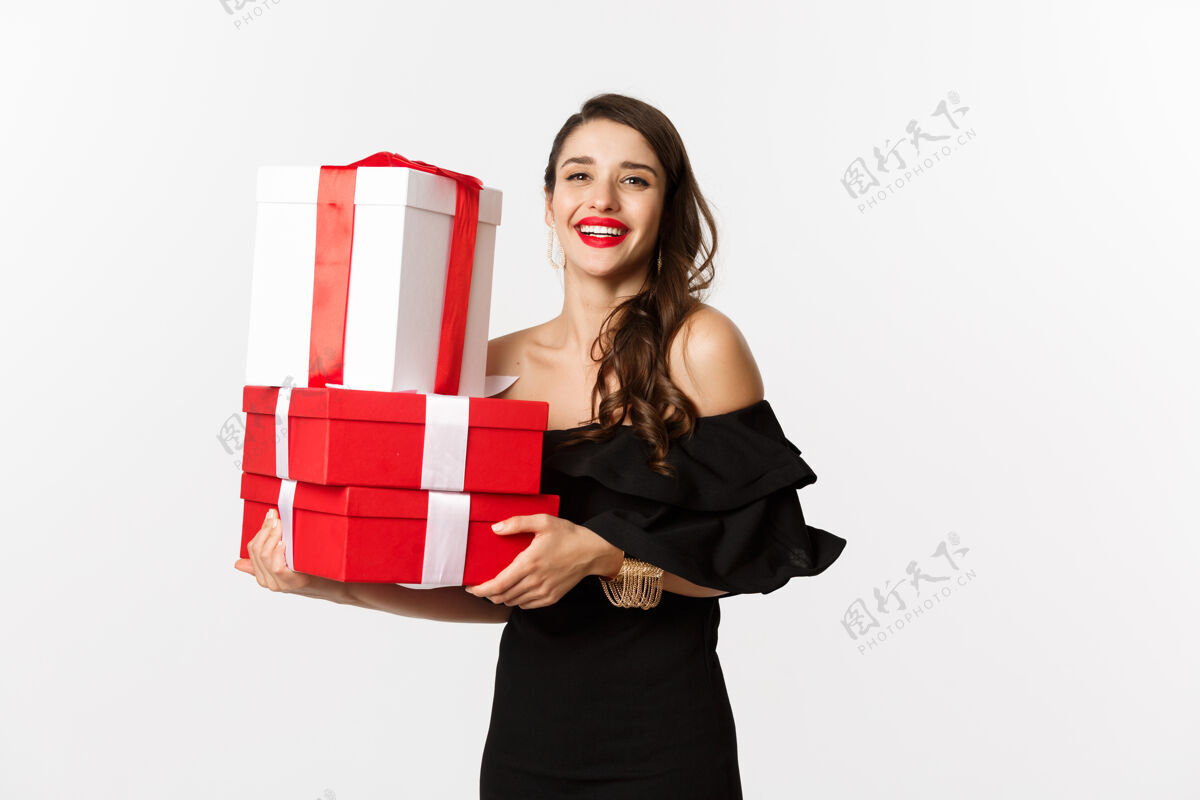 黑发庆祝和圣诞节的概念时尚的女人穿着黑色优雅的裙子 拿着礼物 微笑着 站在白色的背景下唇膏美容长发