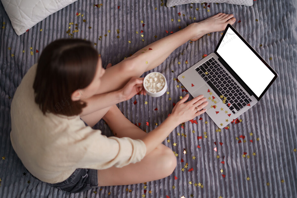 呆在家里美丽的女人和她的家人和朋友在网上庆祝使用笔记本电脑 喝咖啡与五彩纸屑在床上新年网站视频会议
