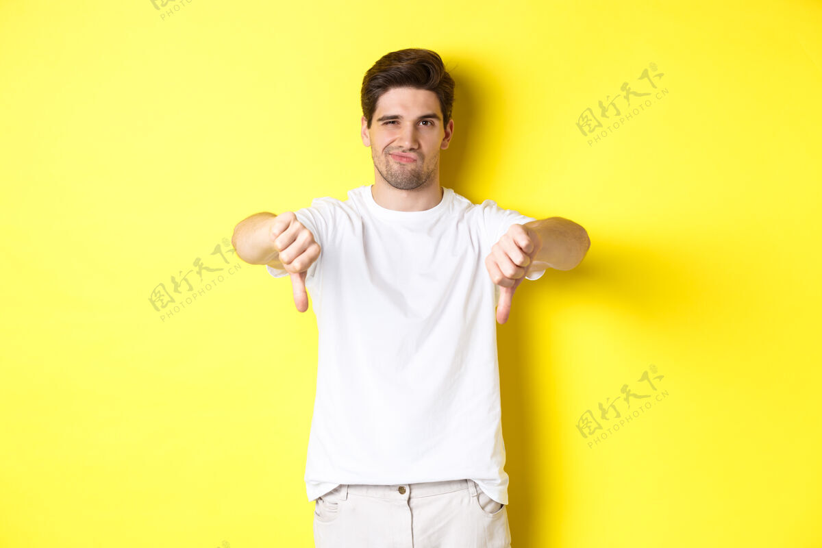 工作室怀疑的家伙竖起大拇指笑着 不喜欢也不同意 站在黄色背景上复制空间年轻成年人男人