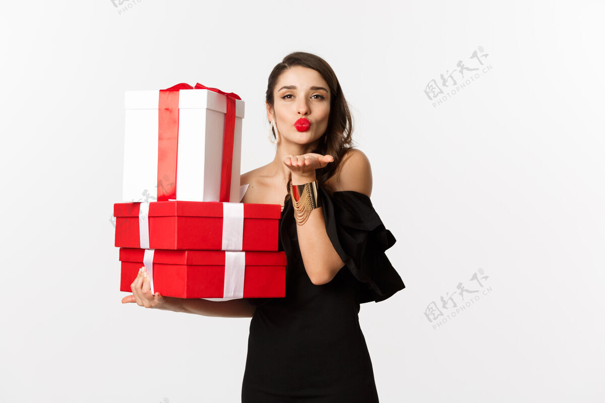 模特庆祝和圣诞假期的概念美丽的女人在优雅的黑色礼服举行的礼物 送在镜头前的空气亲吻 站在白色的背景时装时尚礼品盒