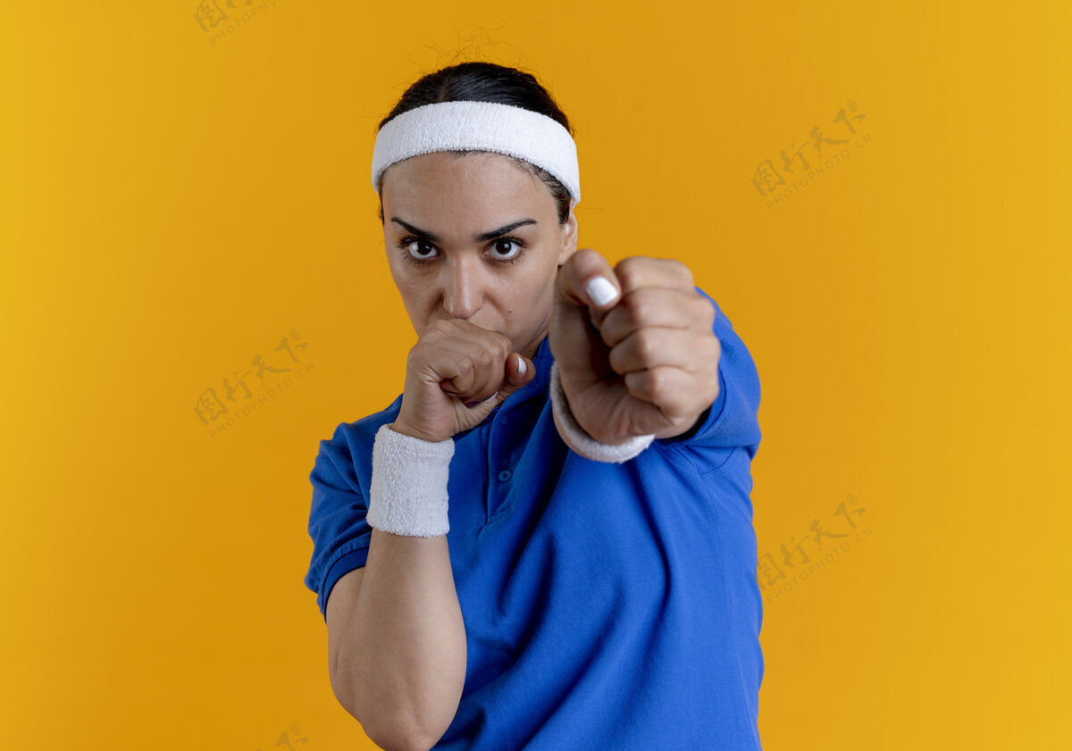 运动年轻自信的白人运动女性戴着头带和腕带保持拳头假装打橙色的复制空间女人戴复制