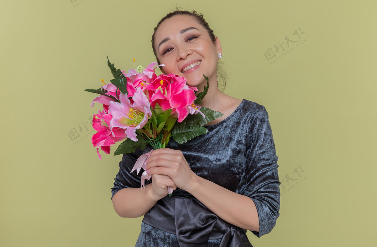 举办快乐的亚洲女人捧着花束 微笑着 站在绿色的墙上 看着前方庆祝国际妇女节花站立亚洲