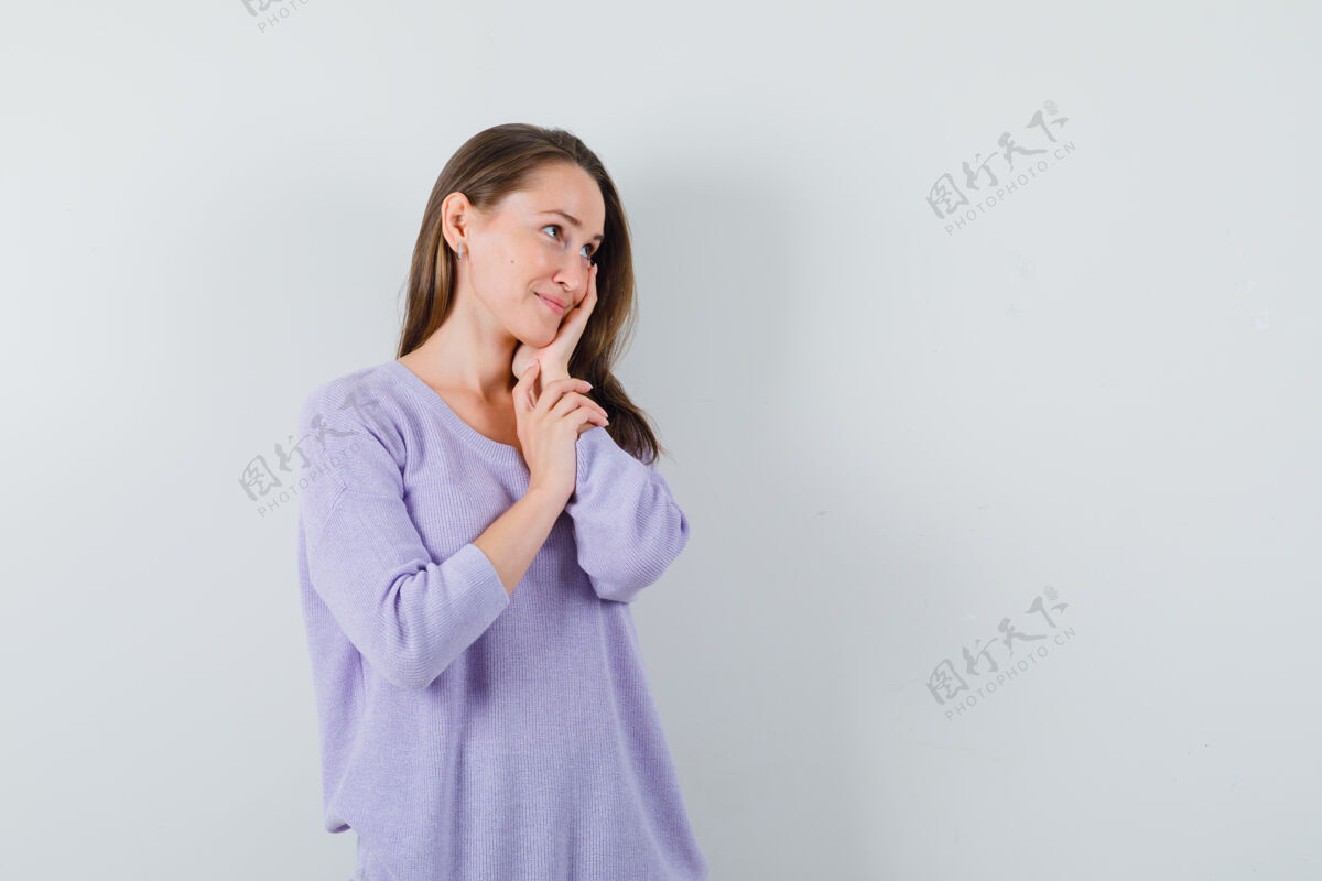 而一个年轻的女人 手放在脸上 一边看着淡紫色的衬衫 一边高兴地看着正视图文本空间女性持有高兴