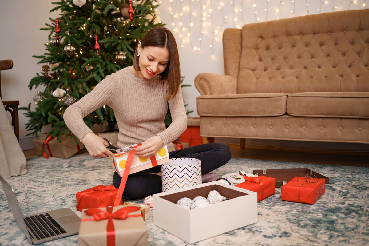 包装女人坐在客厅里的衣柜上包装圣诞礼物笔记本电脑屏幕手