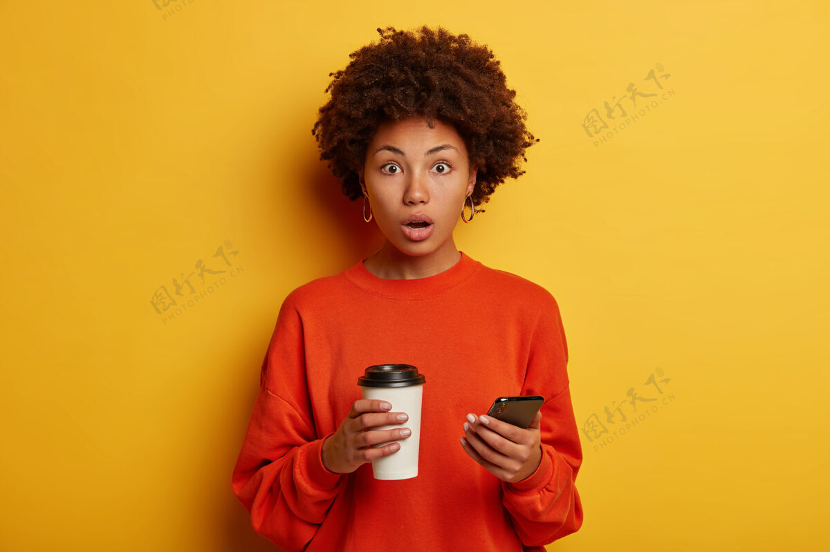 尴尬震惊的少数民族妇女在智能手机上收到令人震惊的信息咖啡惊讶非洲裔