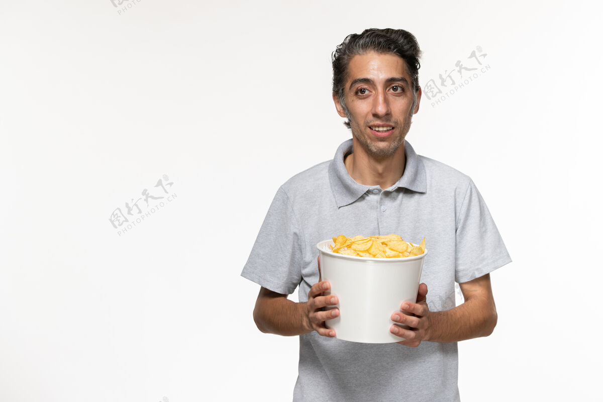 年轻的男正面图年轻男性在白色表面吃薯片电影院杯子遥控