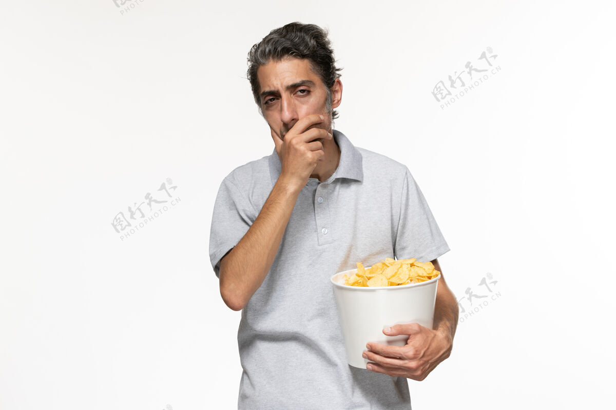 抱正面图年轻的男性拿着土豆片篮子 在白色的表面上思考土豆电影思考