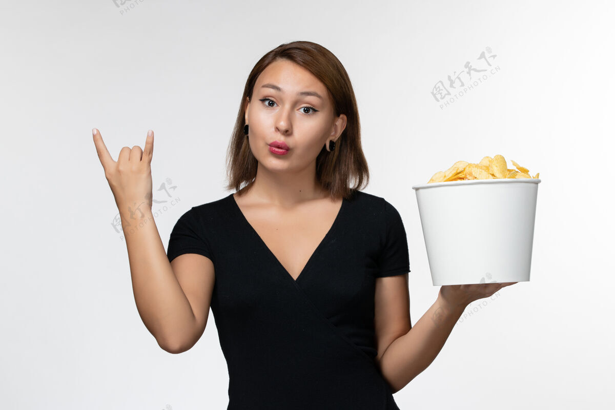 土豆正面图：身穿黑色衬衫的年轻女性在白色表面上拿着薯片前面剧院抱着