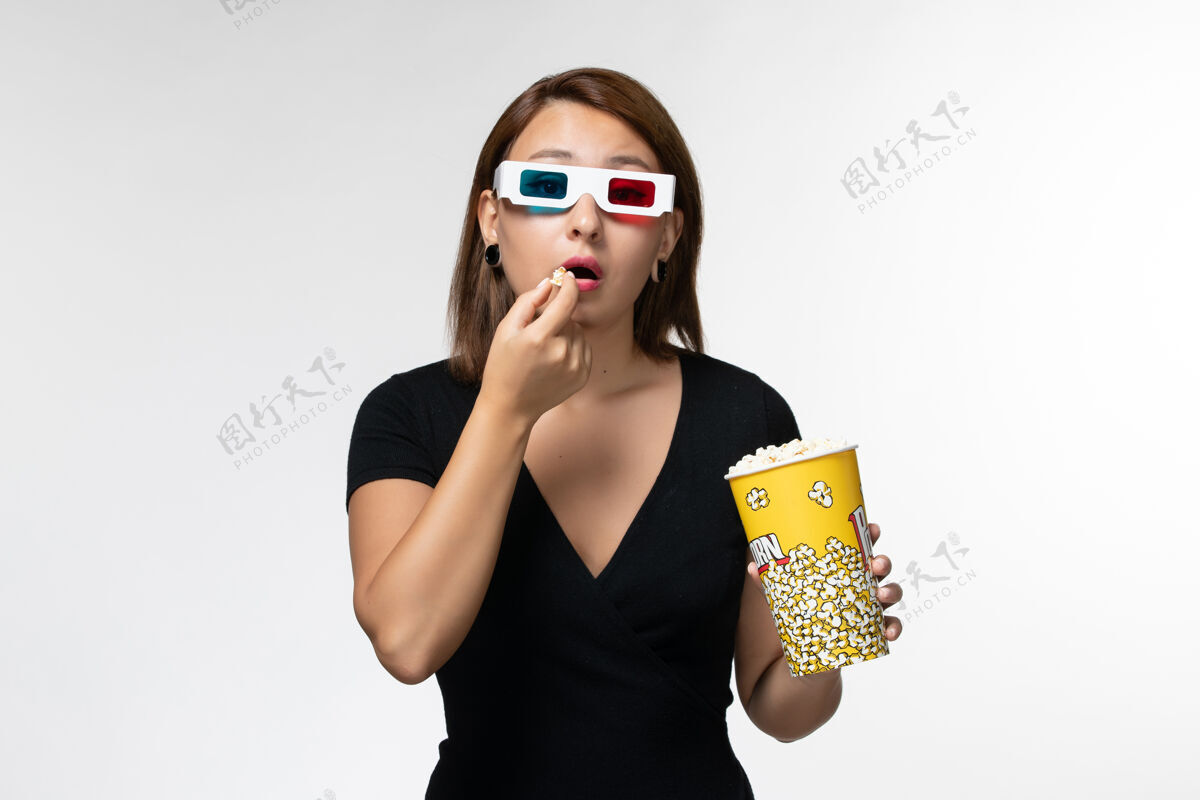电影正面图年轻的女性拿着爆米花 戴着d型太阳镜在白色的地面上看电影太阳镜孤独看