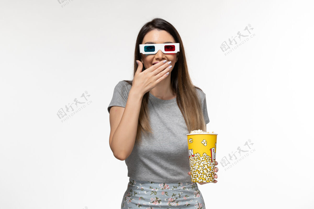 孤独正面图年轻女性手持爆米花 戴着d型太阳镜在浅白色的表面上看电影浅白色抱着太阳镜