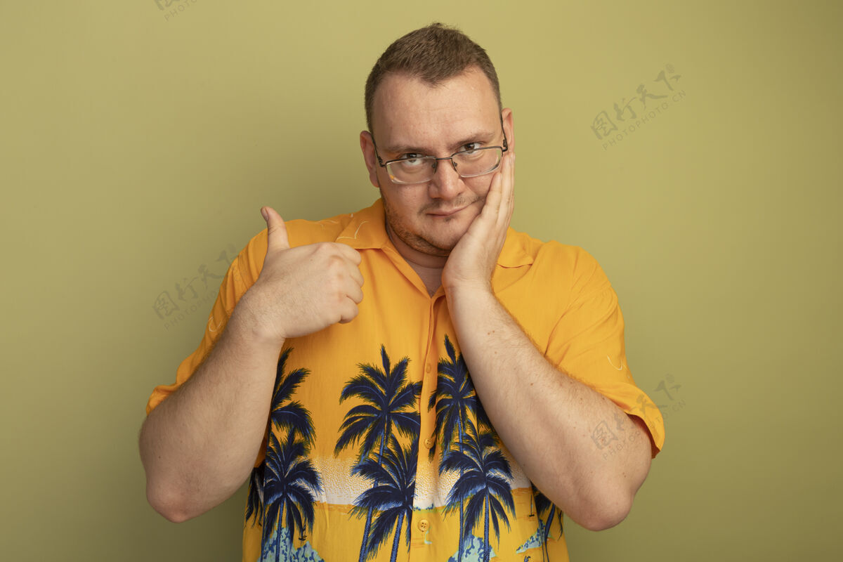 男人一个戴着眼镜 身穿橙色衬衫 竖起大拇指 微笑着站在明亮的墙上的男人站立光拇指