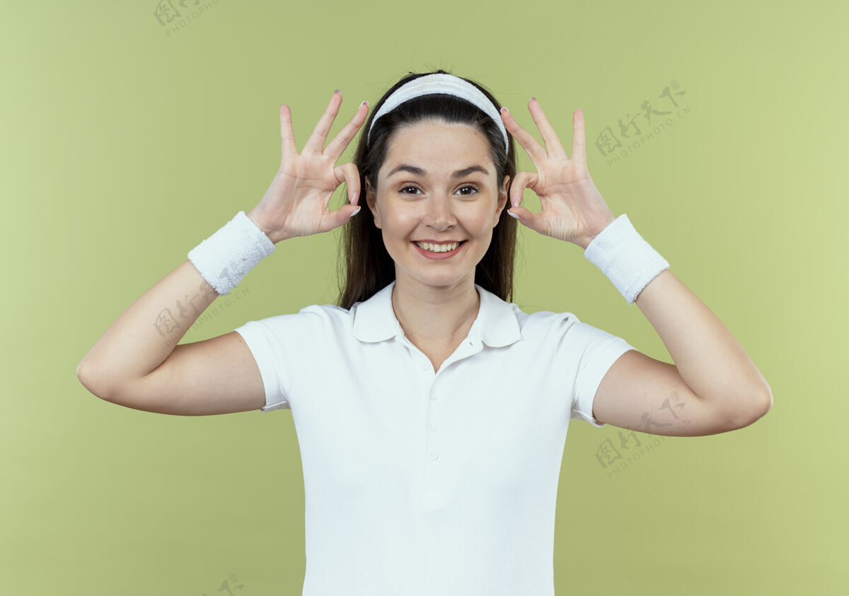 年轻戴着头巾的年轻健身女士微笑着 站在光墙上 露出ok标志欢呼女人好